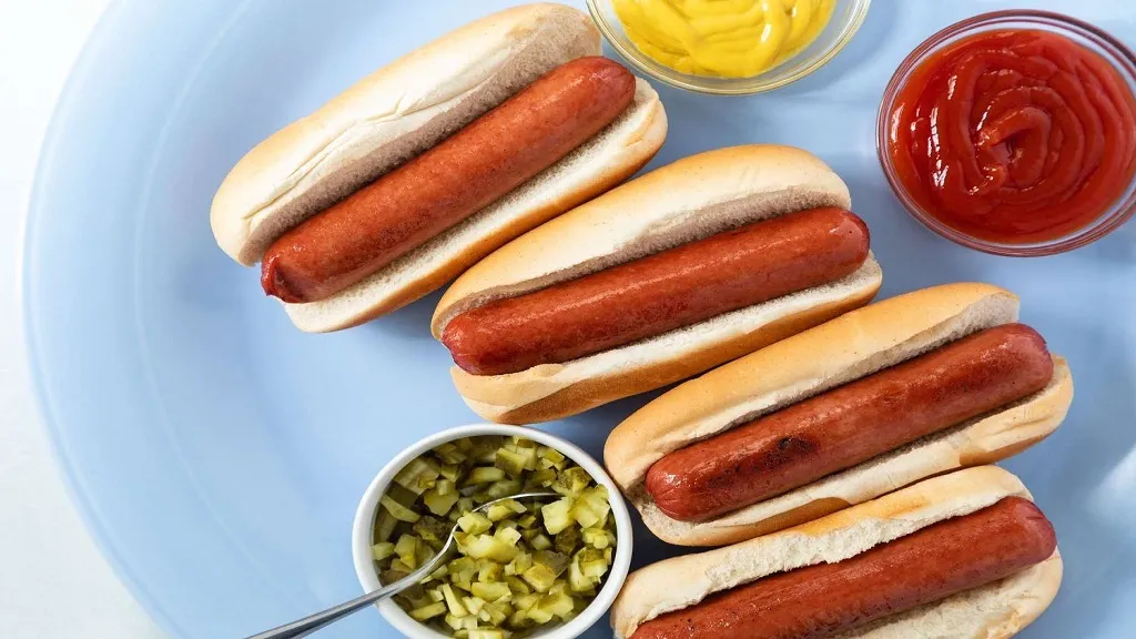 Image of hot dogs on a plate with sides of ketchup, mustard and relish.